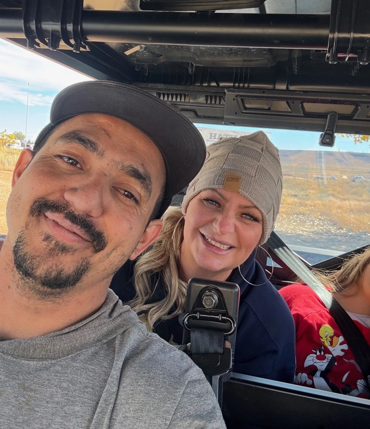 Two people smiling inside a vehicle on a sunny day.