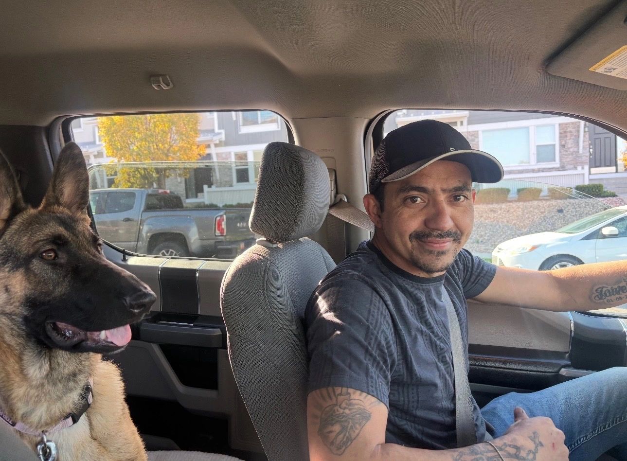 Man driving a car with a German Shepherd dog in the passenger seat.
